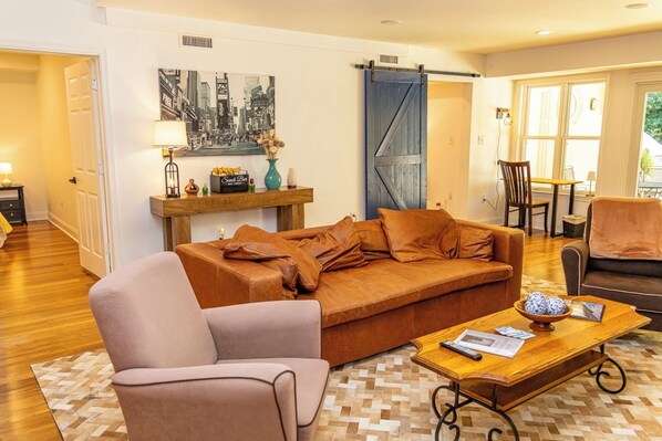 A living room with a sofa, armchair, coffee table, and a painting on the wall.