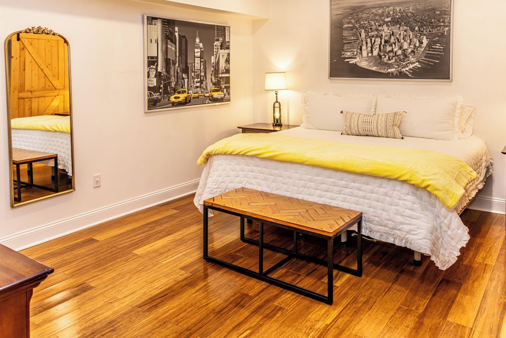 A hotel room with a large bed, a wooden floor, a mirror, and two wall-mounted pictures.