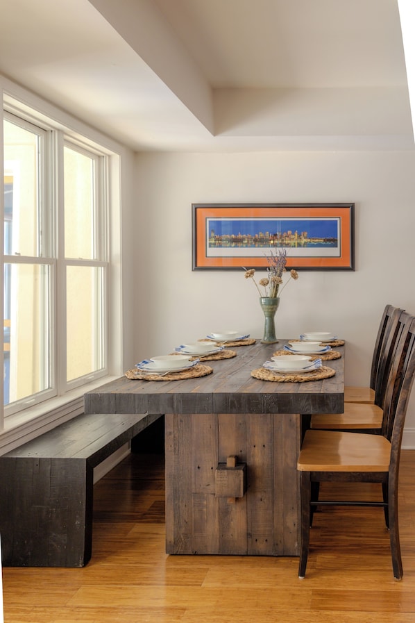 Un comedor con una mesa de madera preparada para cuatro personas, un banco y una silla.
