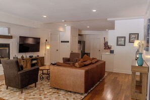 A living room with a sofa, armchair, flat-screen TV, wooden cabinet, and a small table.