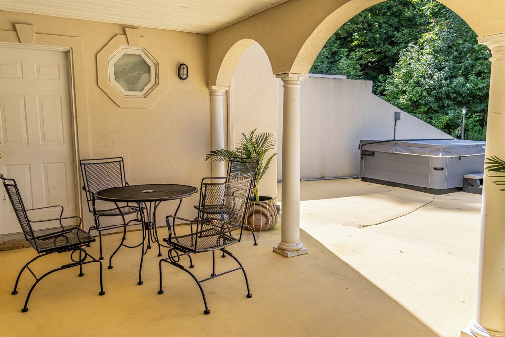Un patio exterior con una mesa redonda y sillas, una planta en maceta y una zona cubierta para la parrilla.