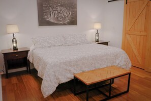Ein Schlafzimmer mit einem Bett, zwei Nachttischen mit Lampen, einer hölzernen Bank, einer Holztür und einem an der Wand hängenden Bild.