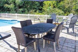 Un patio exterior con una mesa redonda y sillas, una piscina y una valla blanca.