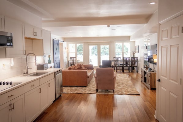 A spacious kitchen with a dining area, wooden flooring, and large windows.