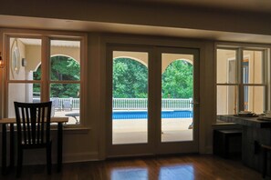 Habitació amb vista a una piscina i arbres, zona de dinar amb taula i cadires, i zona de cuina amb taulell i armaris.