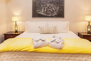 Habitación de hotel con cama, dos lámparas de noche, un cuadro enmarco con vista a la ciudad y dos toallas sobre la cama.