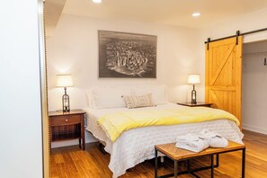 Une chambre à coucher avec un lit, deux tables de chevet, un banc en bois, un grand tableau et une porte coulissante de style grange.