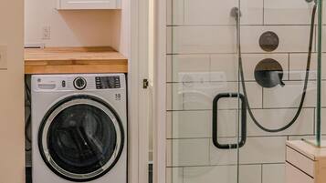 A compact laundry area with a washing machine and a glass-enclosed shower.