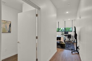 Ein modernes Interieur mit einer weißen Tür, einem Bett mit weißer Bettdecke, einem Schreibtisch und einem Computermonitor.