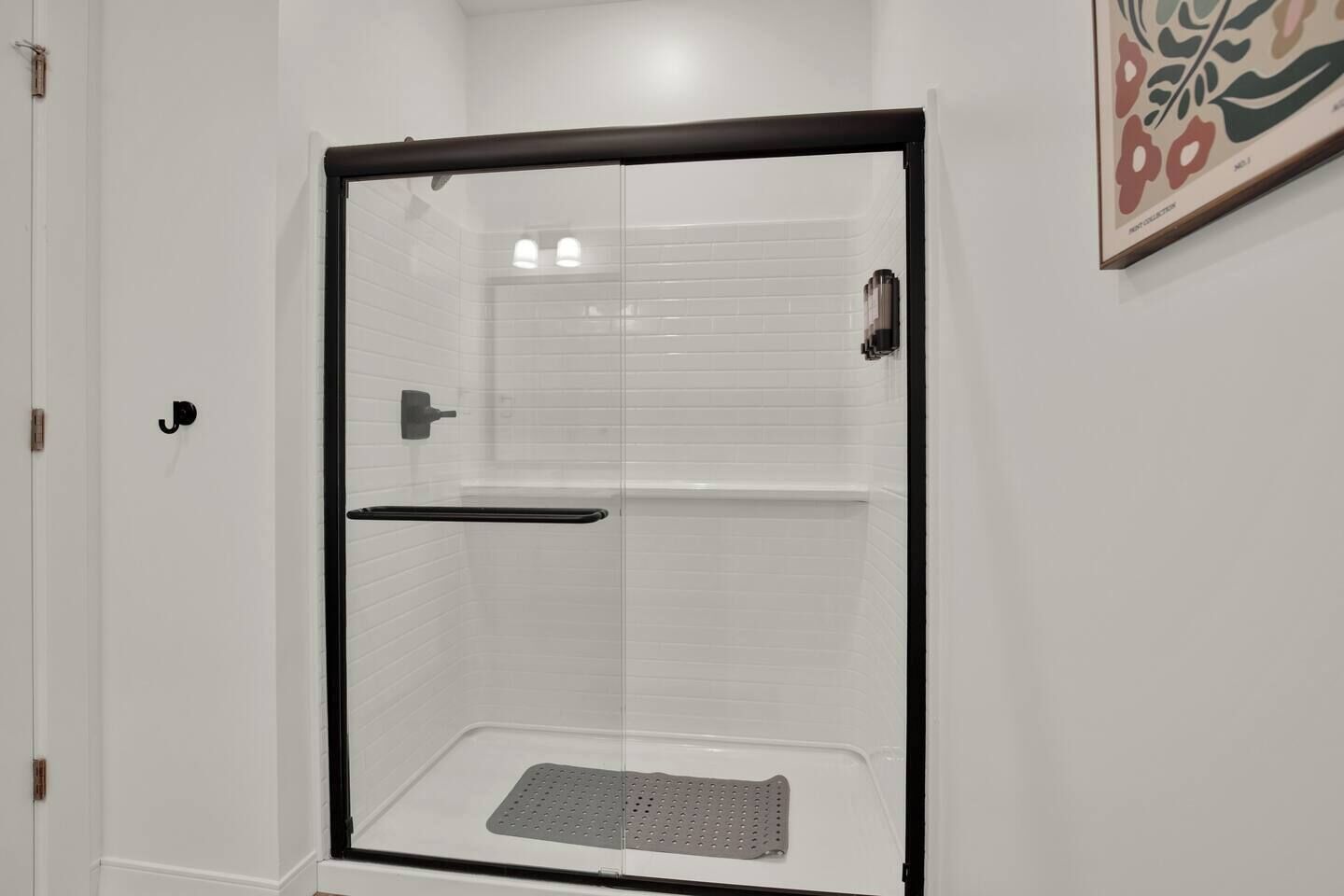A glass-enclosed shower with a black frame, a white tiled wall, and a door with a handle.