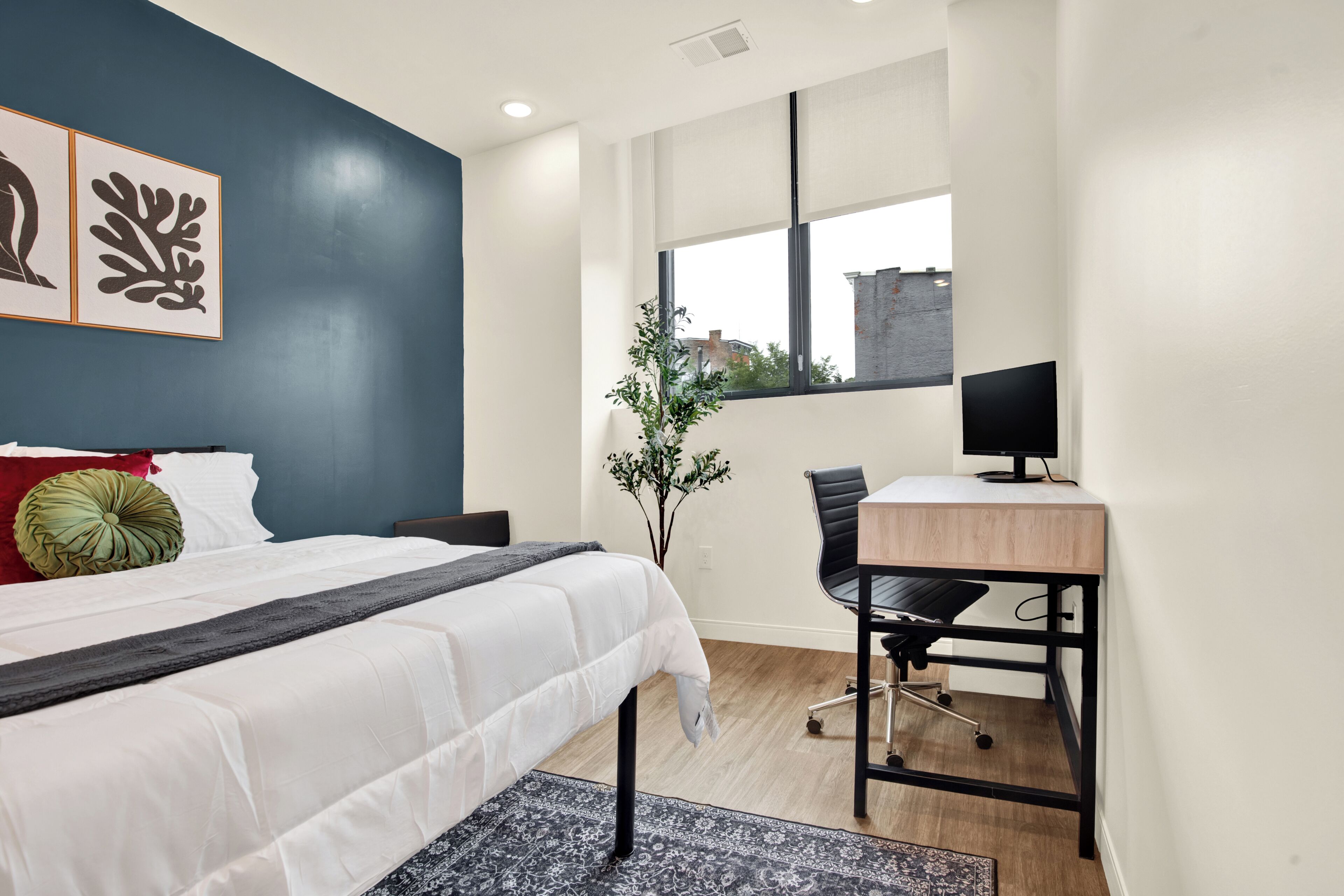 A modern hotel room with a bed, desk, and large window.