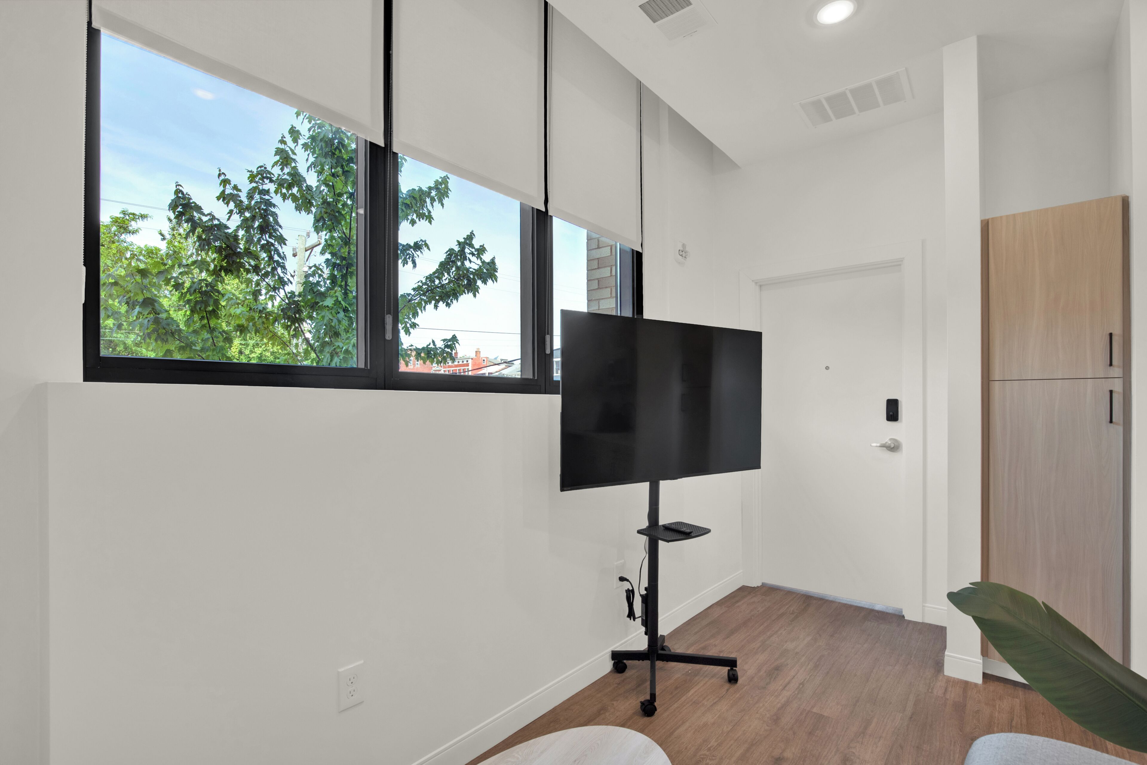 Quarto moderno com uma janela ampla, televisão de tela plana em um suporte, uma porta e um armário de madeira.