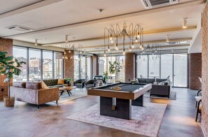 A spacious living area with a pool table, comfortable seating, large windows, and a city view. - Stylish 2BR Suite OTR, Gym, Pool Downtown Access (Cincinnati)