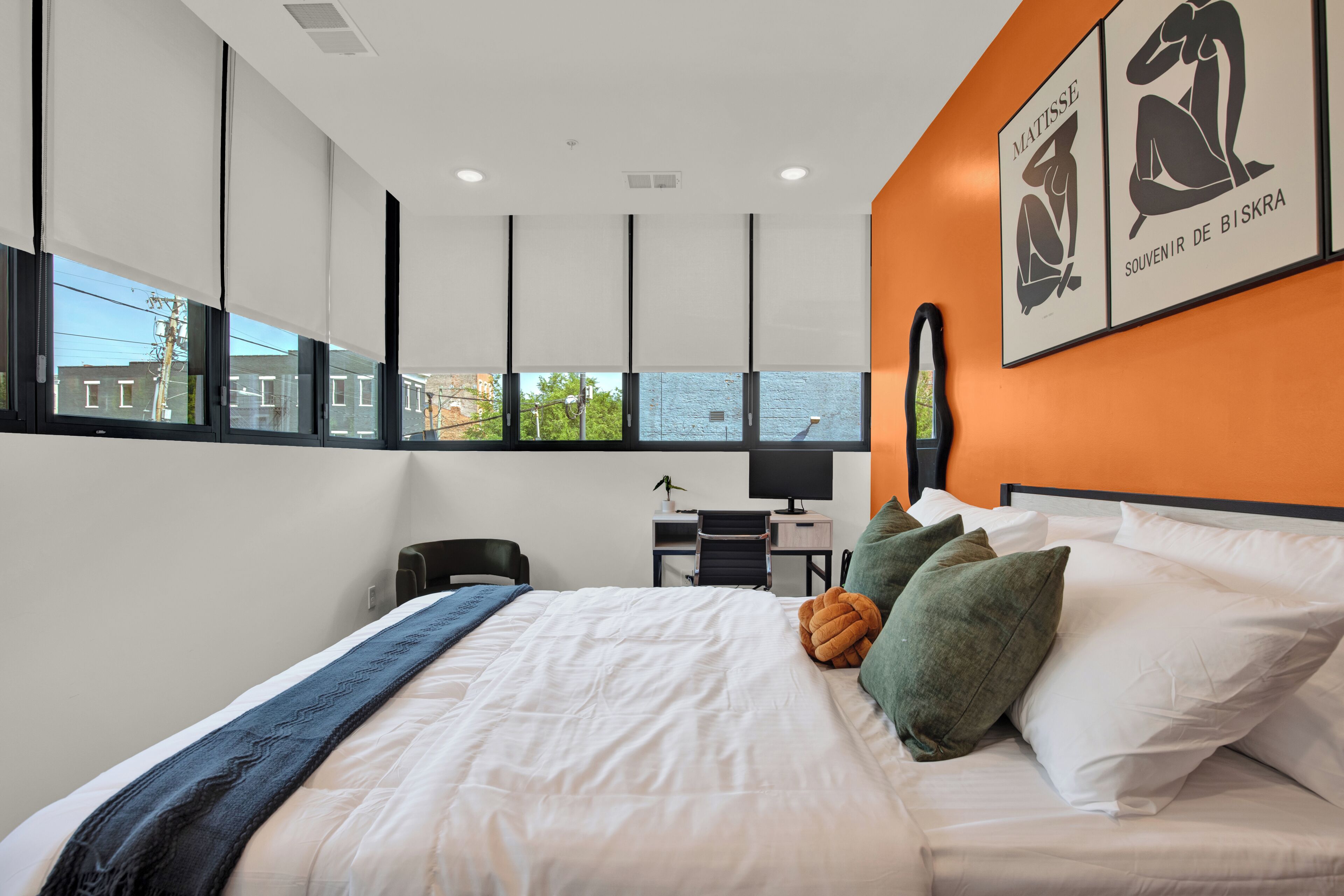 Een moderne hotelkamer met een groot bed, een bureau en uitzicht op de stad door grote ramen.