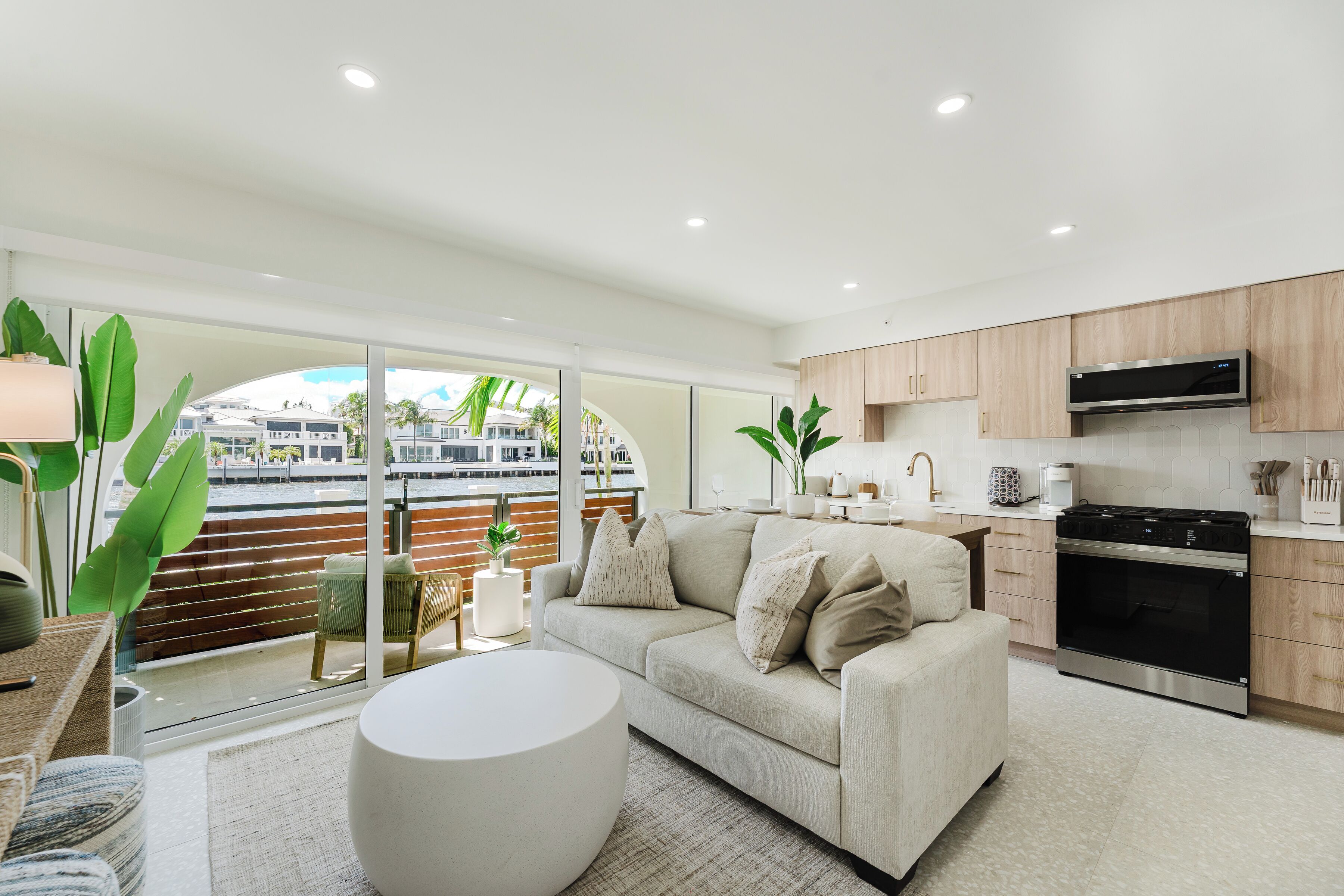 A modern kitchen with a built-in oven and microwave, a beige sofa, and a large window overlooking a cityscape.