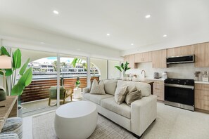 Eine moderne Küche mit Backofen und Mikrowelle, ein beiges Sofa und ein großes Fenster mit Blick auf eine Stadtlandschaft.