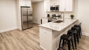 Una cocina moderna con una isla central, electrodomésticos de acero inoxidable y taburetes de bar.
