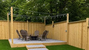 Un patio trasero con una terraza de madera, un brasero y mobiliario para exterior.