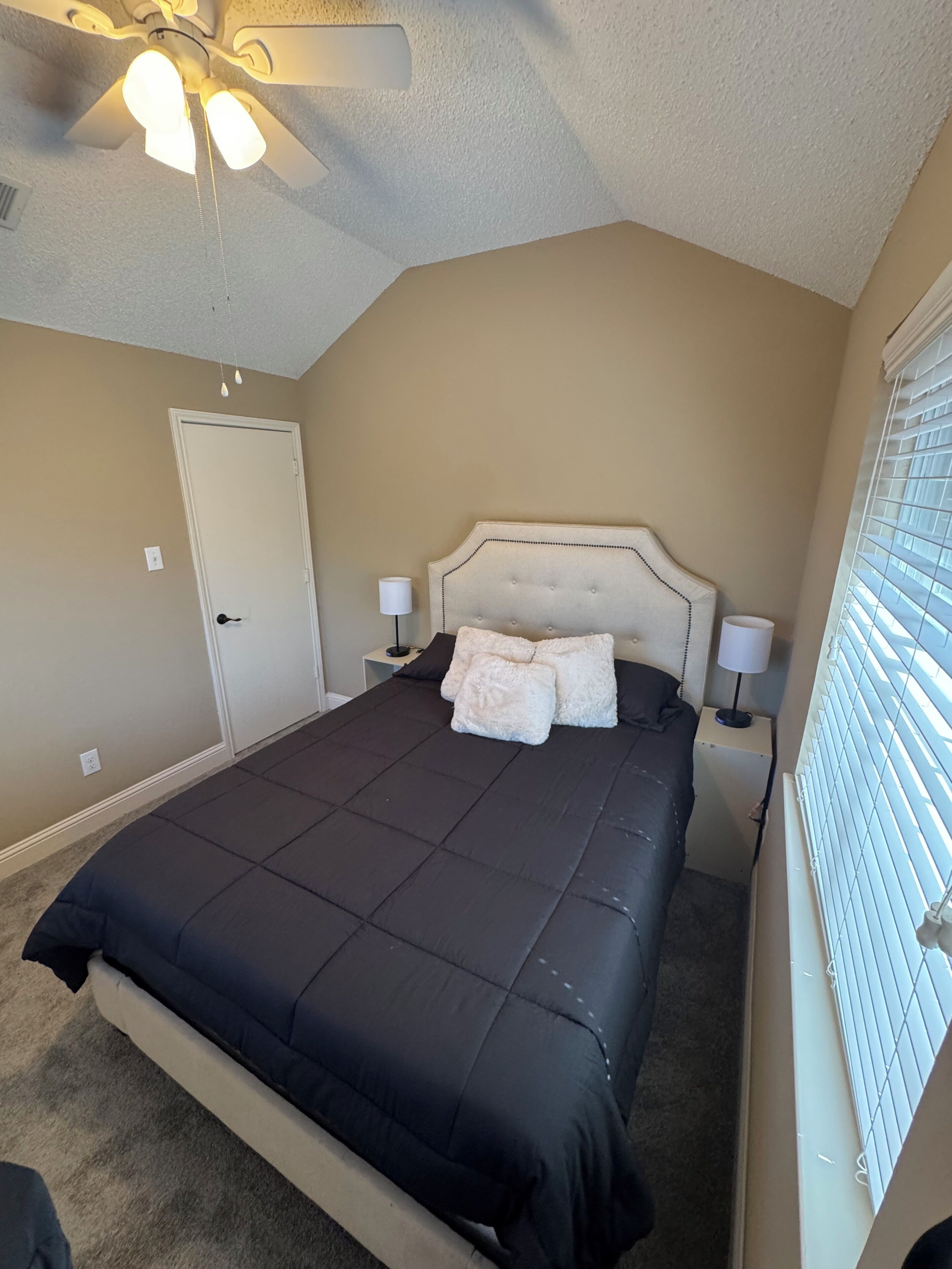 Un dormitorio con cama, ventilador de techo, puerta y ventana con persianas.