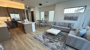 Ein modernes Wohnzimmer mit grauem Sofa, Couchtisch und Essbereich mit Tisch und Stühlen.