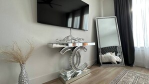 Ein modernes Zimmer mit einem wandmontierten Flachbildfernseher, einem großen Spiegel und einem dekorativen silbernen Konsolentisch.