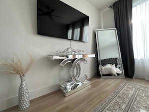 Ein modernes Zimmer mit einem wandmontierten Flachbildfernseher, einem großen Spiegel und einem dekorativen silbernen Konsolentisch.