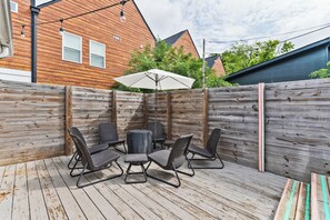 Eine Holzterrasse mit Gartenmöbeln, darunter ein Tisch und Stühle, sowie ein weißer Sonnenschirm.