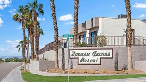 A sign for Havasu Dunes Resort with a clear view of the surrounding area, including a road and palm trees.