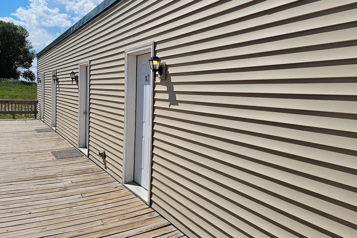 Un bâtiment avec un revêtement extérieur horizontal, une terrasse en bois et trois portes d’extérieur.