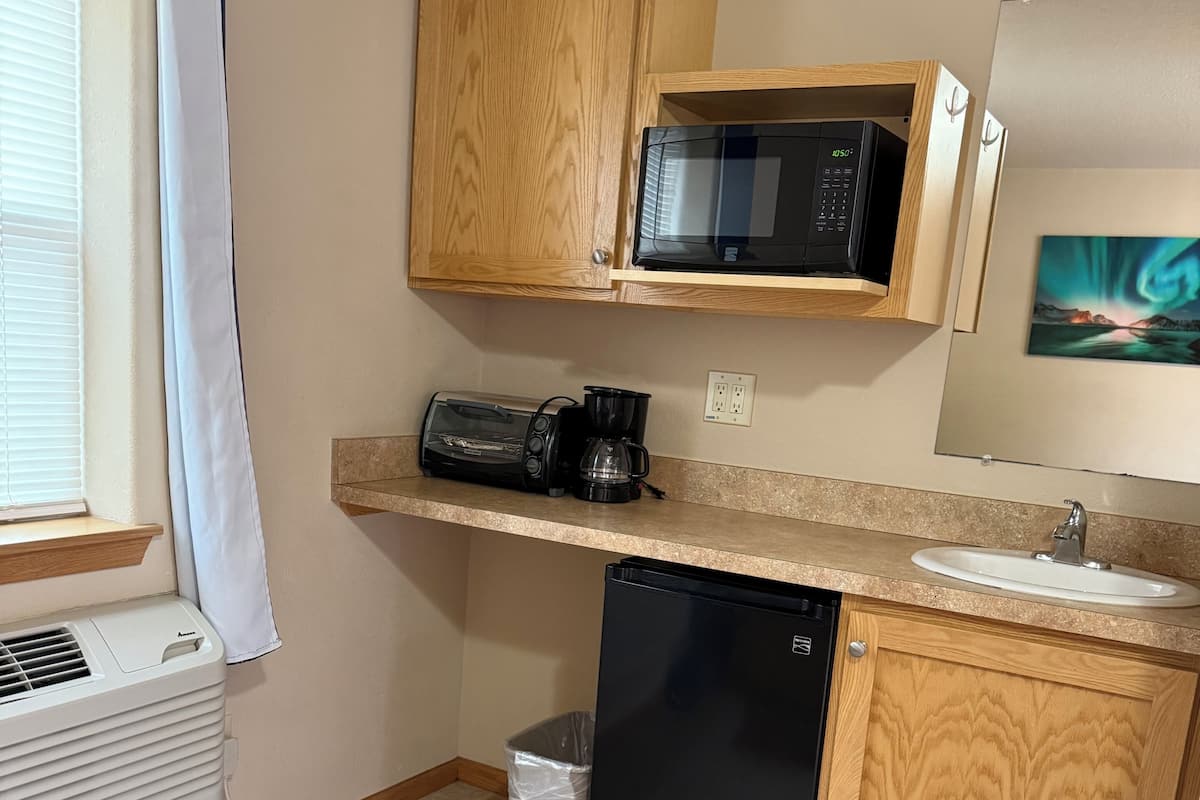 Une cuisine compacte équipée d’un four à micro-ondes, d’un grille-pain et d’une machine à café sur le plan de travail, ainsi que d’un lave-vaisselle et d’une poubelle.