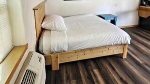 Un dormitorio con cama de madera, televisor montado en la pared, calefactor y suelo de madera.