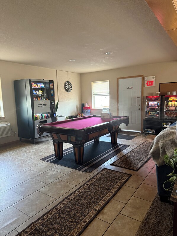 A pool table in a room with a vending machine, dartboard, and a door marked 'EXIT'.