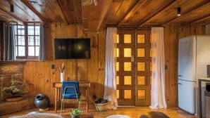 Interior acogedor de una cabaña con techo de madera, televisor de pantalla plana, un sillón azul, un sofá y un refrigerador.