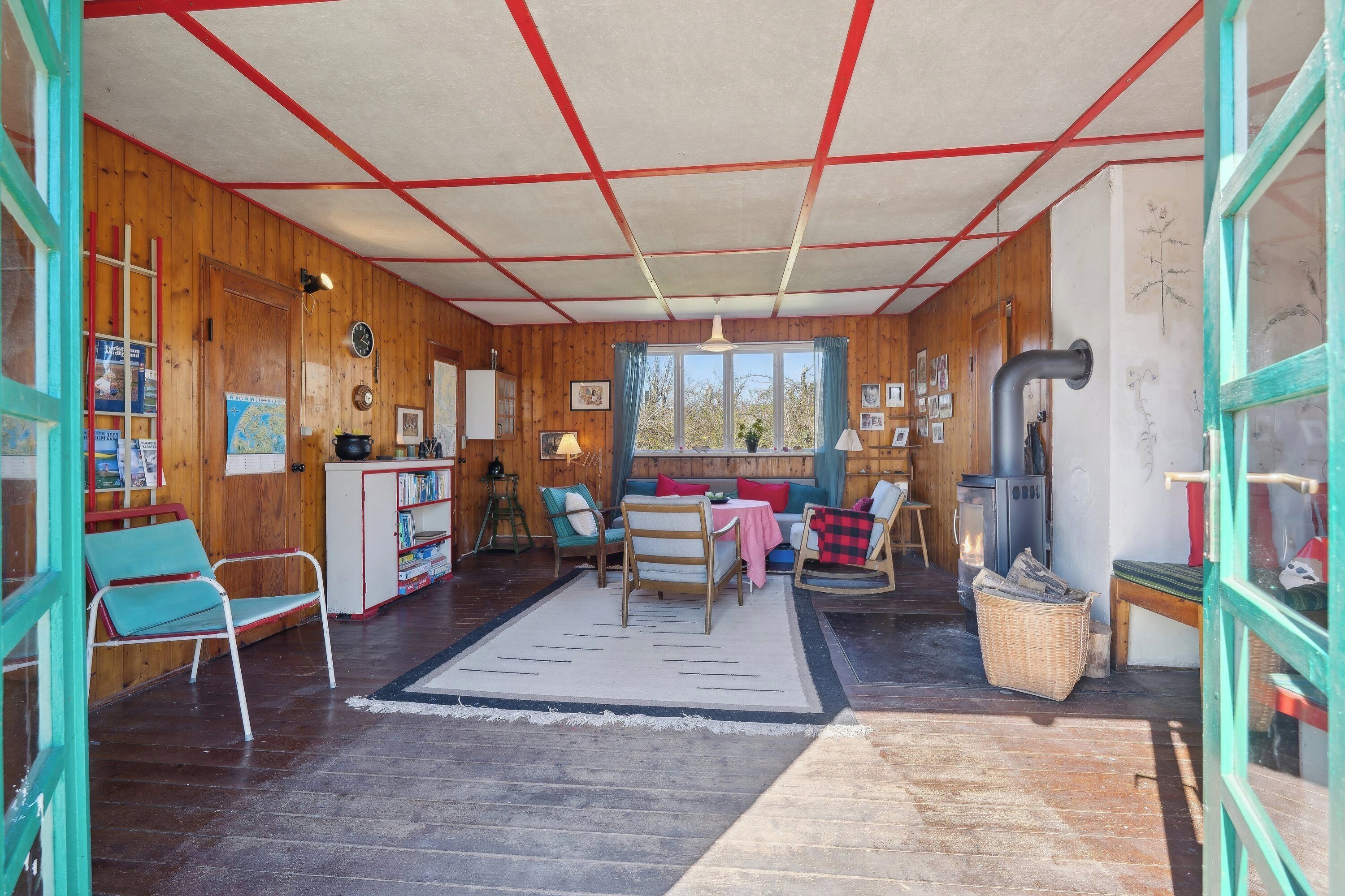 A cozy cabin interior with wooden walls, a sofa, chairs, a table, and a fireplace.