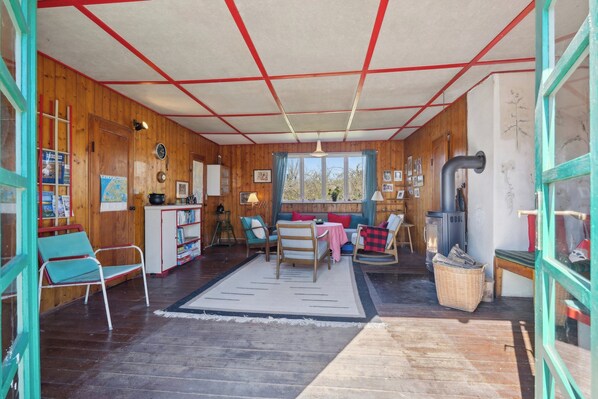 Ein gemütliches Blockhäuschen im Inneren mit Holzwänden, einer Couch, Sesseln, einem Tisch und einem Kamin.