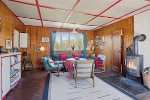 Ein gemütliches Blockhaus-Interieur mit Holzausstattung, einer Sitzecke mit Tisch, einem Bücherregal und einem Kaminofen.