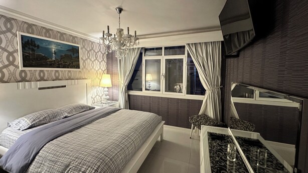 A bedroom with a bed, a bedside table with a lamp, a window with curtains, a chandelier, and a wall-mounted picture. - Vacation Rental (La Paz)