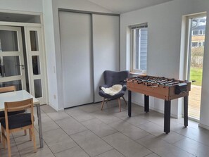 A room with a foosball table, a chair, a table, and a sliding door. - 4 Star Holiday Home in Grenaa (Grenaa)