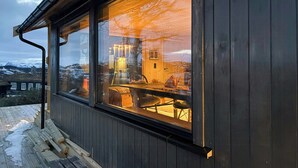 Eine Holzfassade mit einem großen Fenster, das einen Raum mit einem Chandelier und einem Tisch reflektiert.