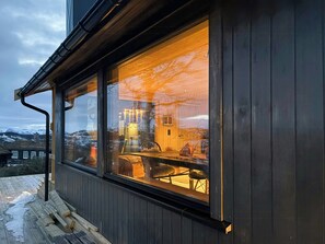 A wooden exterior wall with a large window reflecting a room with a chandelier and a table. - Cottage by Rauland ski trails with annex (Rauland)
