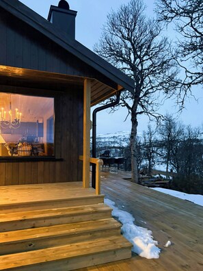 A wooden staircase leading to a room with a large window, a chandelier, and a view of a snowy landscape. - Cottage by Rauland ski trails with annex (Rauland)