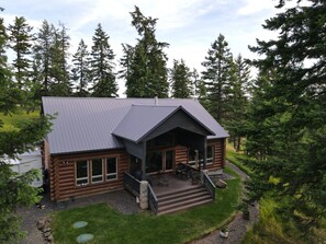 Een vakantiehuis van hout met een metalen dak, een veranda met zitplaatsen en uitzicht op een bebost gebied.