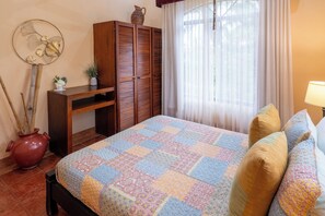 Ein Schlafzimmer mit einem Bett, einem Holzschrank, einem kleinen Tisch mit einer Vase und einem Fenster mit Vorhängen.