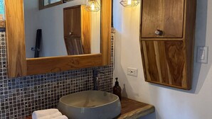 Ein Badezimmer mit einem Holz-Waschtisch, einem großen Spiegel, einem Aufsatzwaschbecken und einer gefliesten Spritzschutzwand.