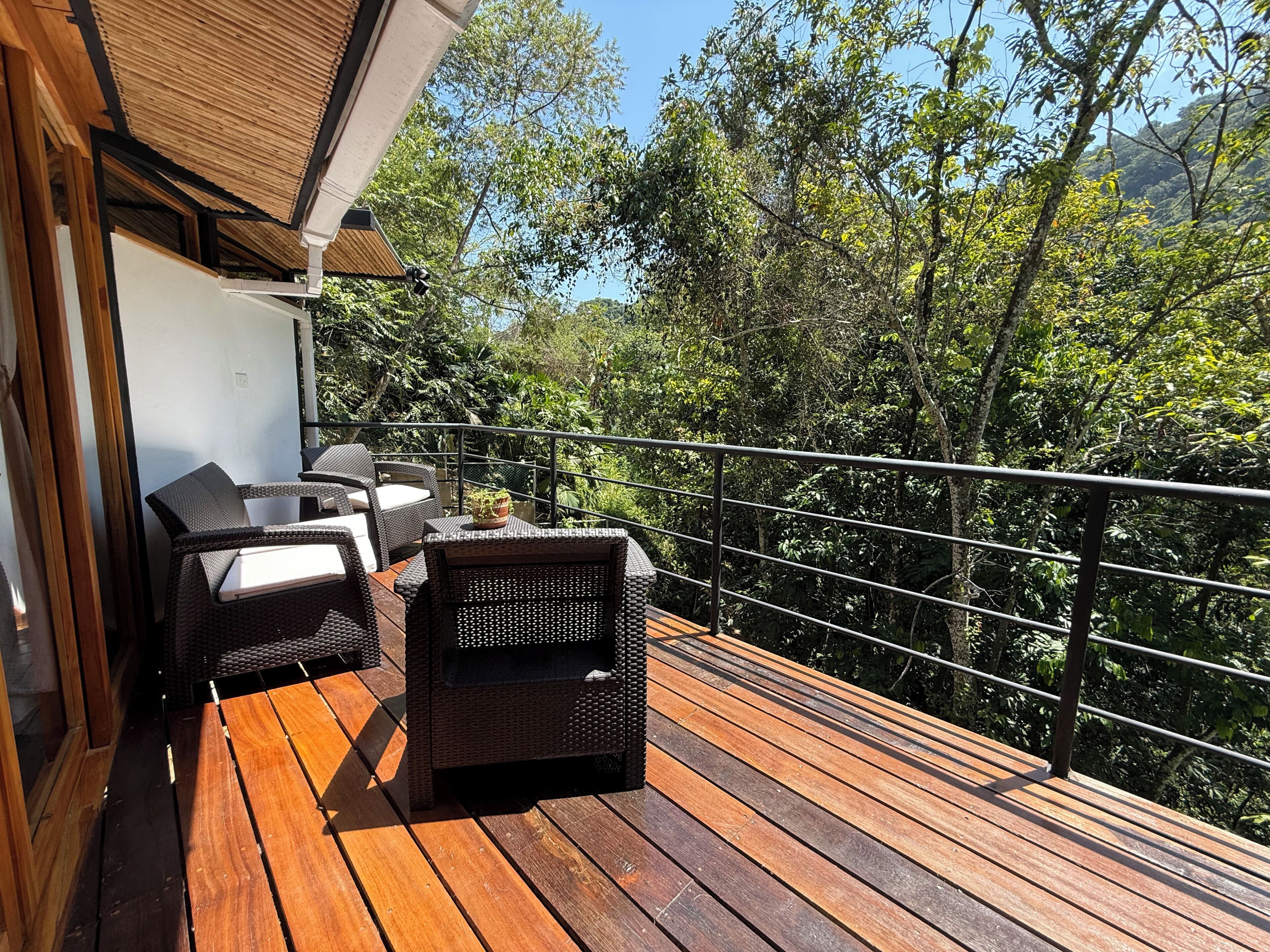 A wooden deck with outdoor furniture, a railing, and a view of dense greenery.