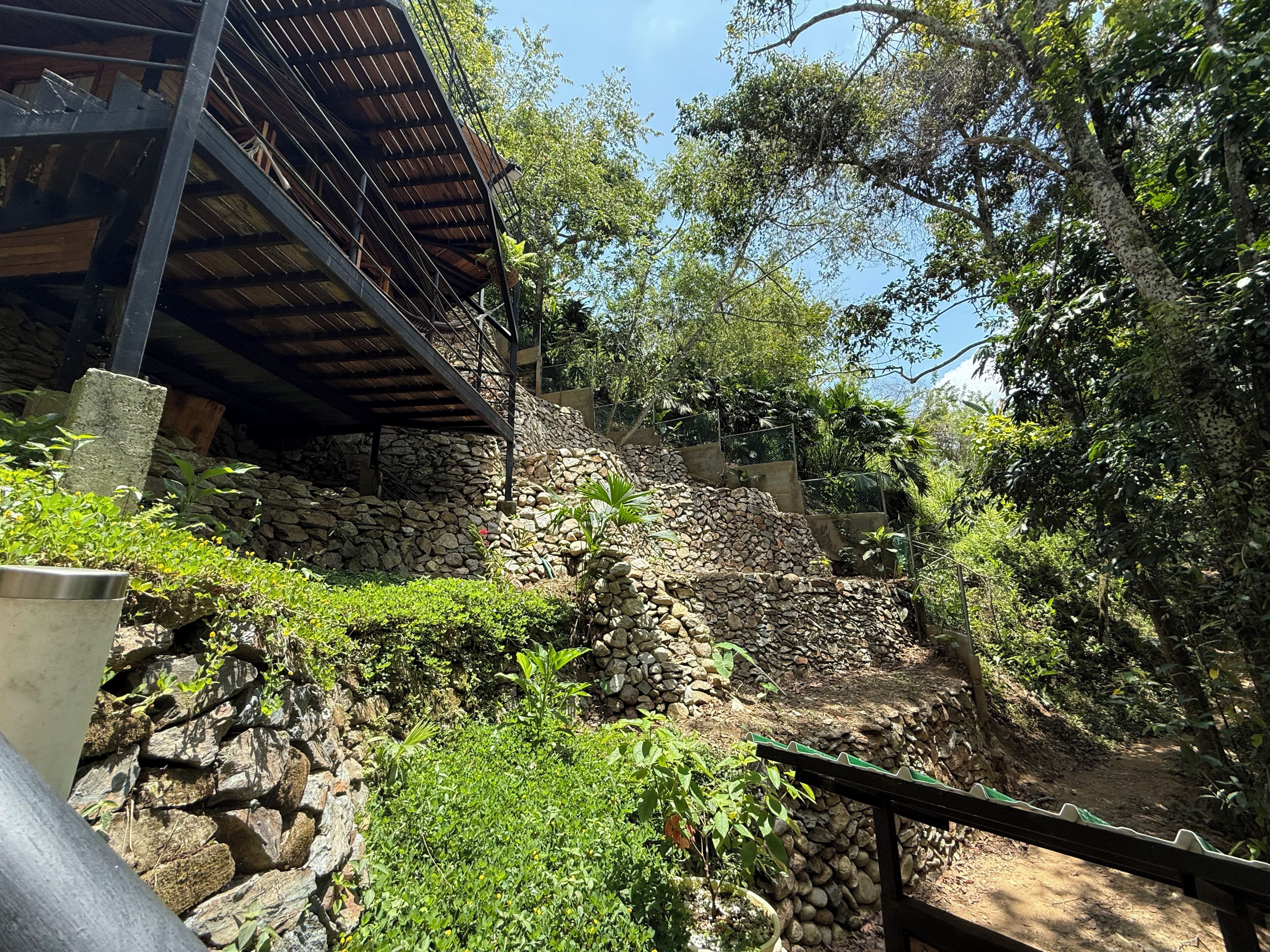 Un muro de piedra con una escalera que sube hacia un edificio con techo metálico.