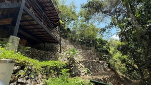 Eine steinerne Stützmauer mit Grünpflanzen, eine Metalltreppe und ein Holzbau.