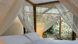Ein Bett mit weißer Bettwäsche, einem Baldachin und Blick auf Grün.