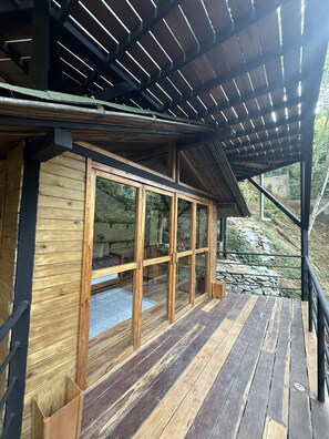 Una cabaña de madera con puertas de cristal amplias, una terraza de madera y una estructura de techo de metal.