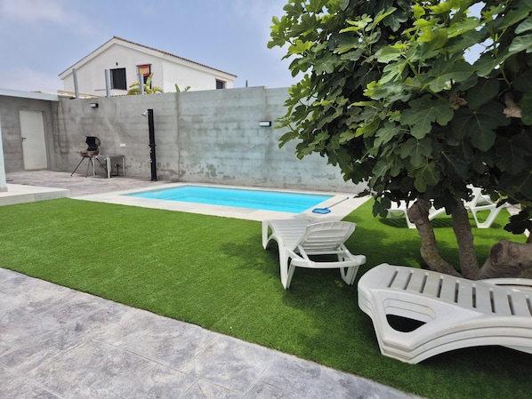 A swimming pool with artificial grass, white lounge chairs, and a tree. - Lola's Little House (Conil de la Frontera)